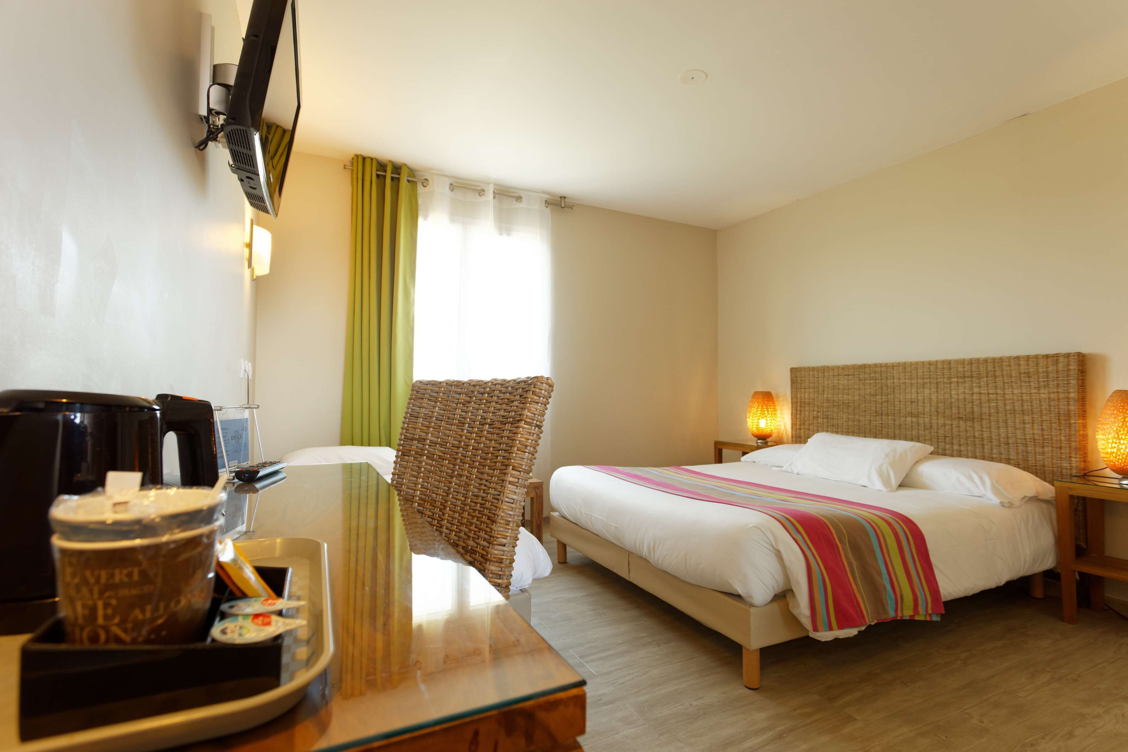 A hotel room with a bed, bedside tables, a coffee machine, a wicker chair, and curtains.