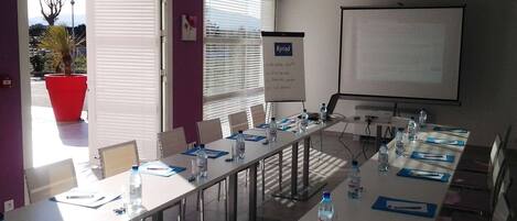 A conference room with a long table, chairs, a projector screen, and a whiteboard.