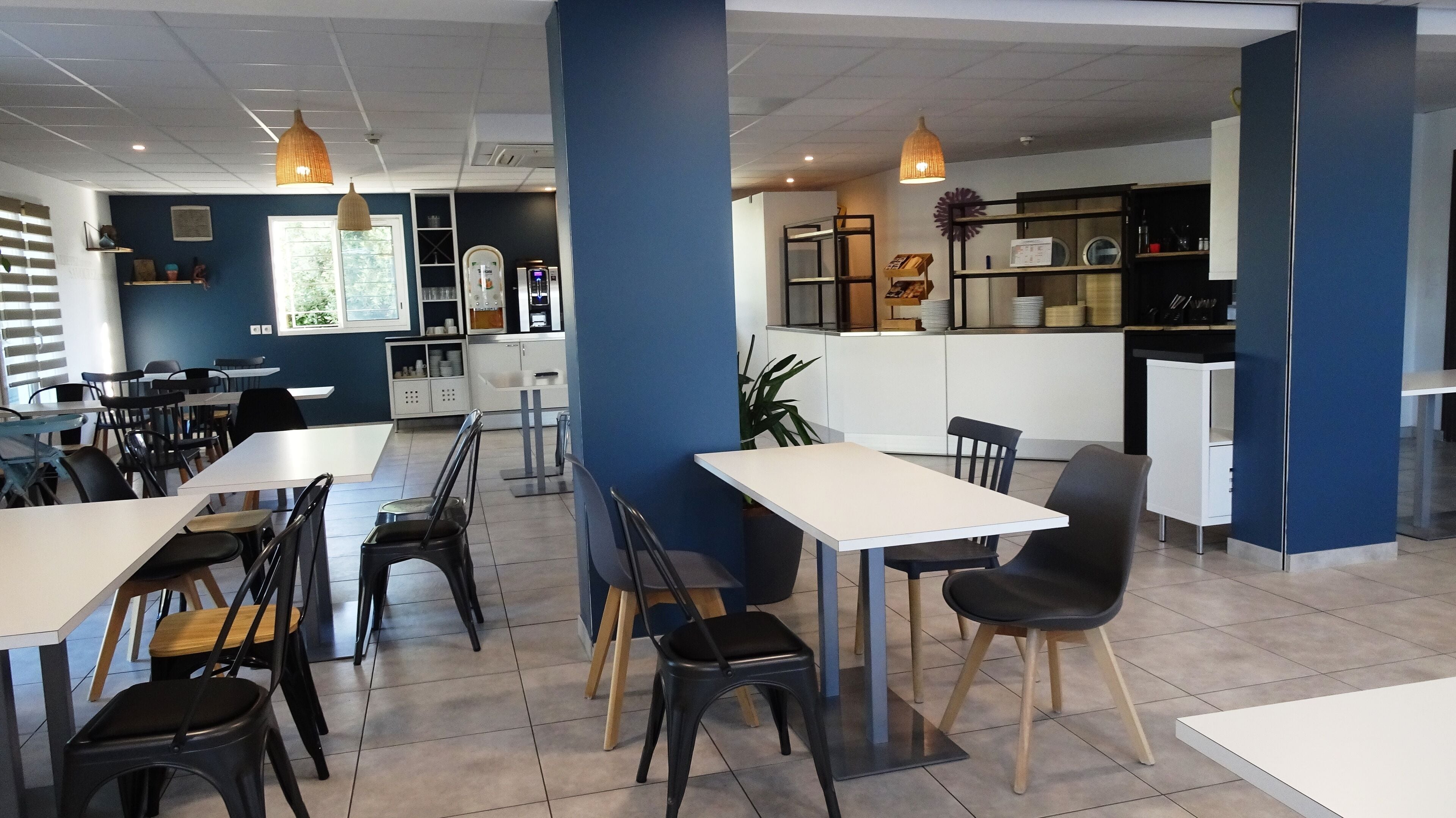 A modern dining area with tables and chairs, a kitchen area, and a counter with a menu.