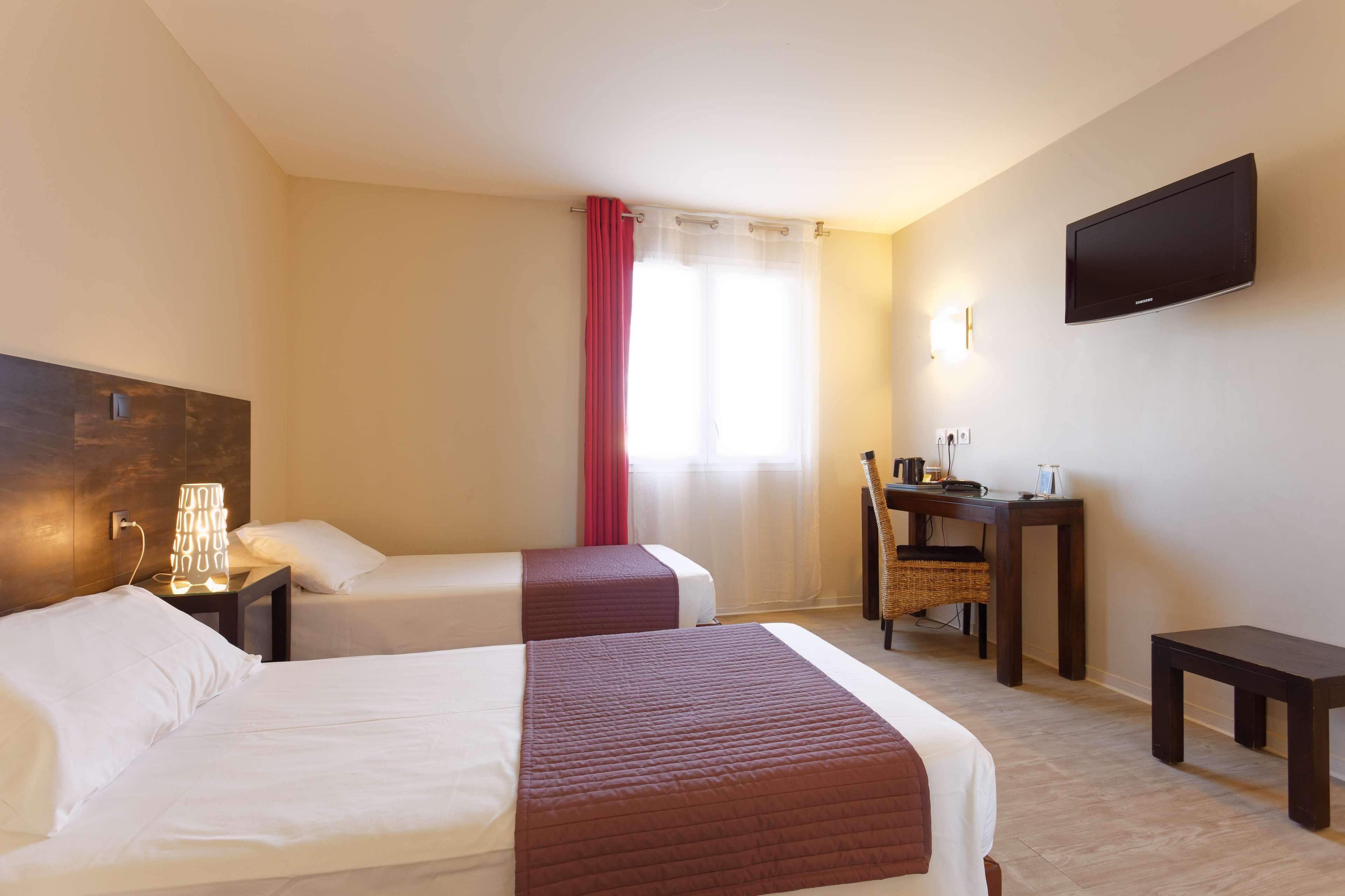 Habitación de hotel con dos camas, un escritorio, una silla, un televisor y una ventana con cortinas.