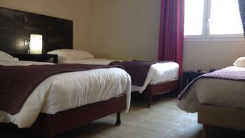 A hotel room with two beds, a wooden headboard, a nightstand with a lamp, and a window with red curtains.