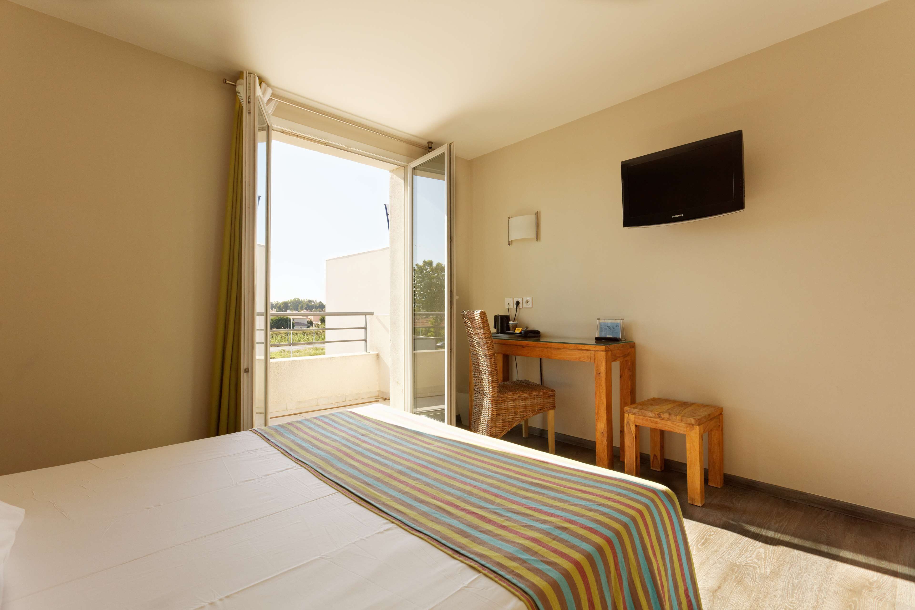 Une chambre d’hôtel avec un lit, un bureau, une chaise, une télévision et un balcon avec vue.