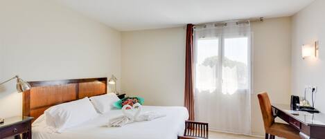 Une chambre d’hôtel avec un grand lit, un bureau, une chaise et une fenêtre avec des rideaux.