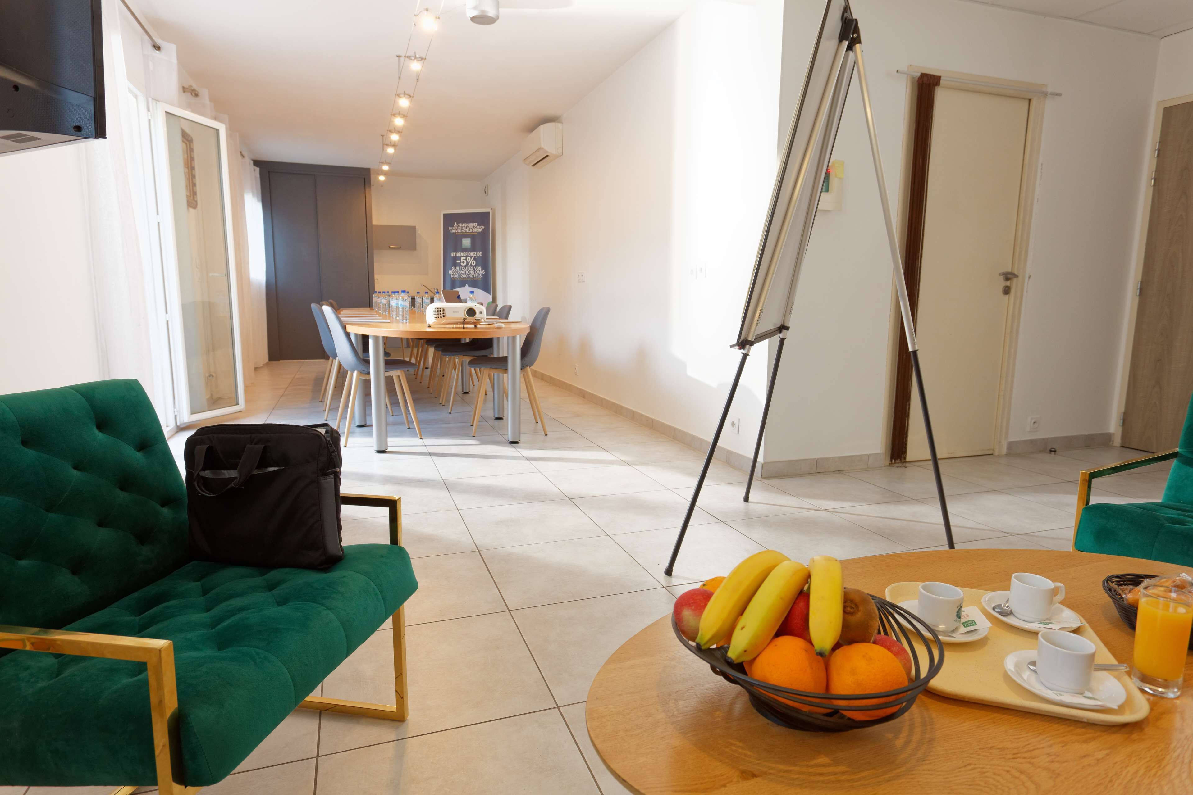 A modern hotel room with a green sofa, a dining table with chairs, a fruit bowl, and a breakfast tray.