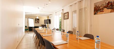 A conference room with a long wooden table, chairs, water bottles, and a painting on the wall.