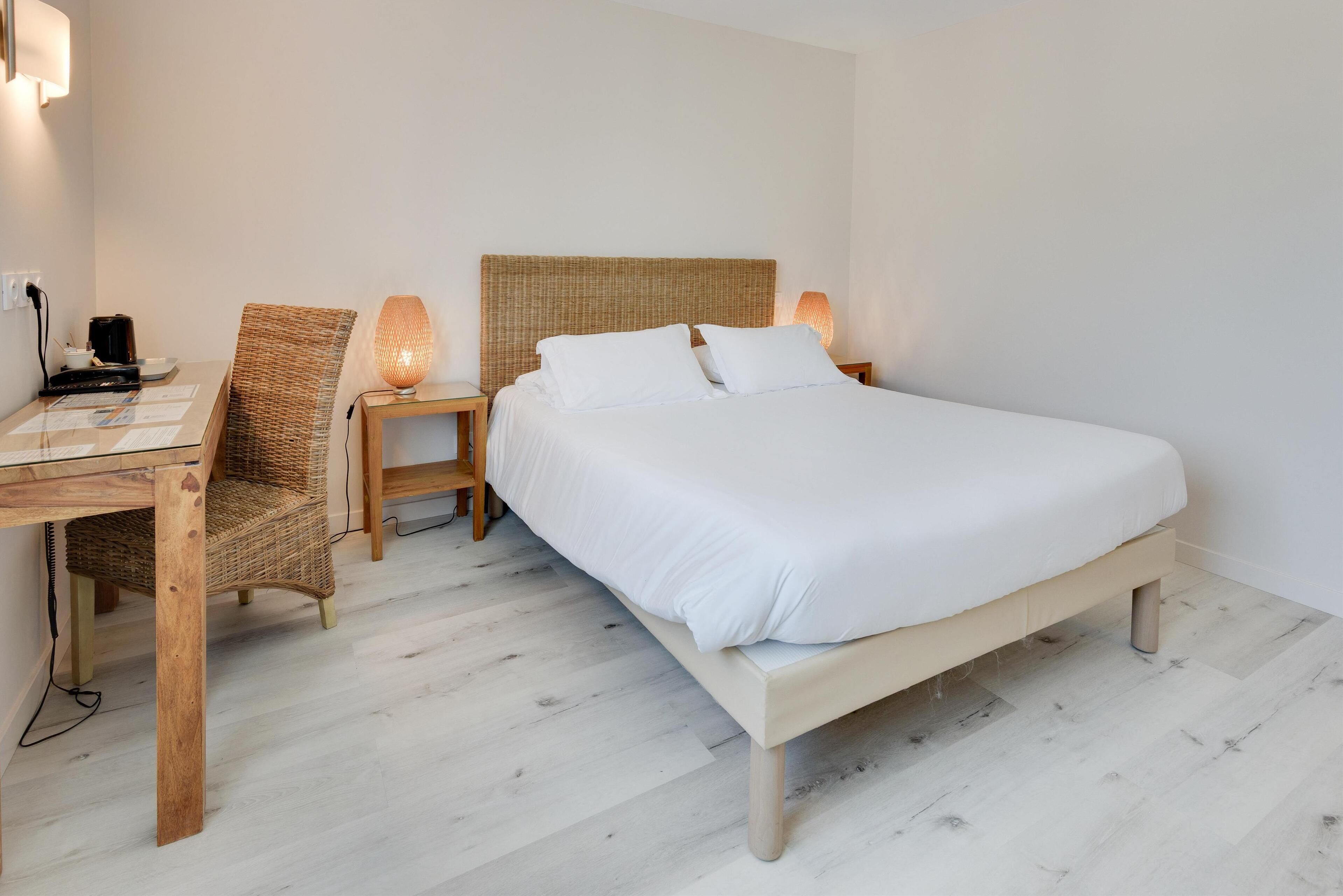 A neatly arranged bedroom with a bed, a desk, a chair, and a nightstand with a lamp.