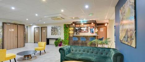A lobby with a green sofa, yellow chairs, a round table, and a bar area with blue chairs.