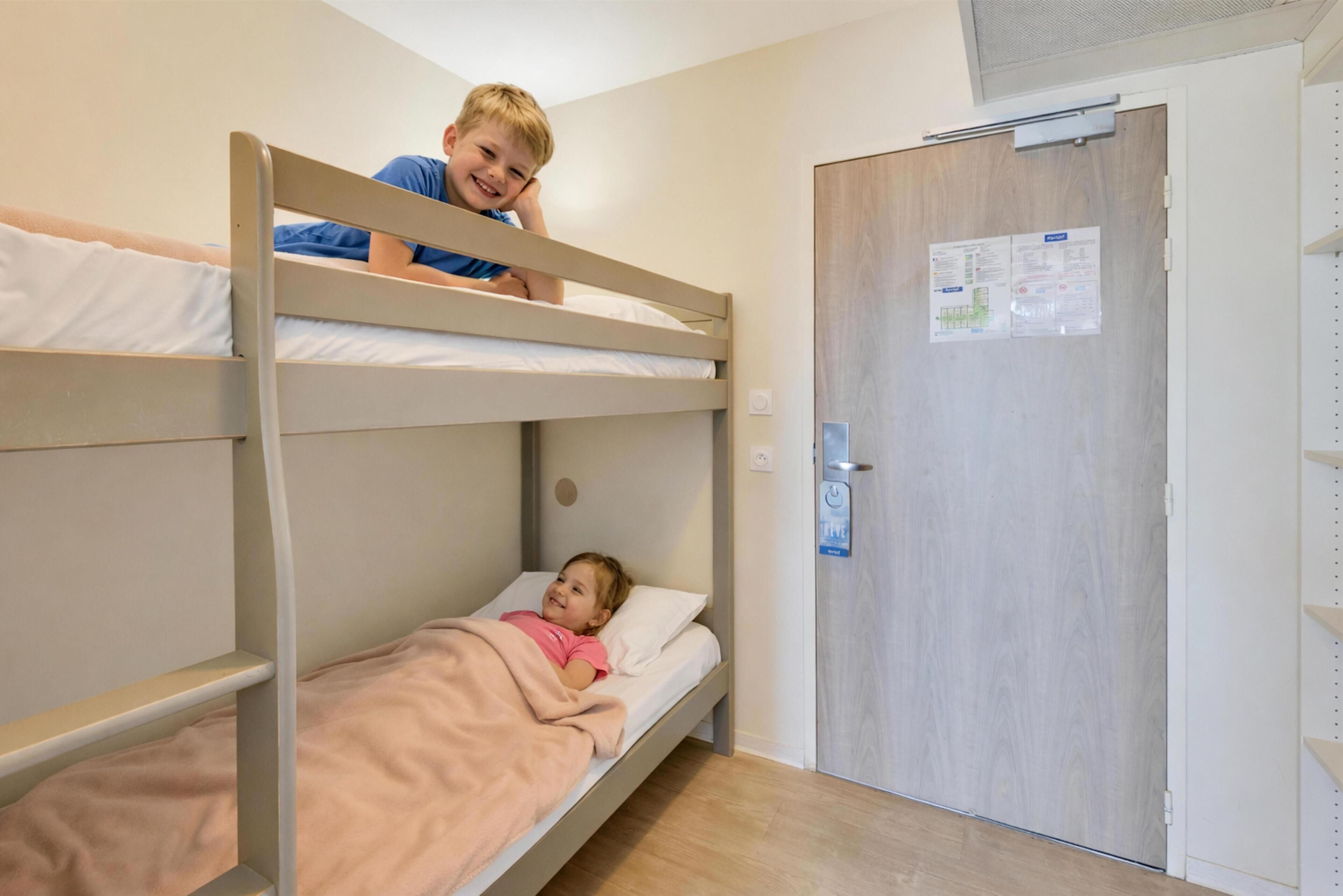 Une chambre avec un lit superposé, une porte en bois et un tableau d’affichage.