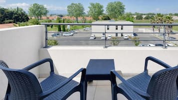 Un balcón con dos sillas y una mesa, con vistas a un aparcamiento y edificios.