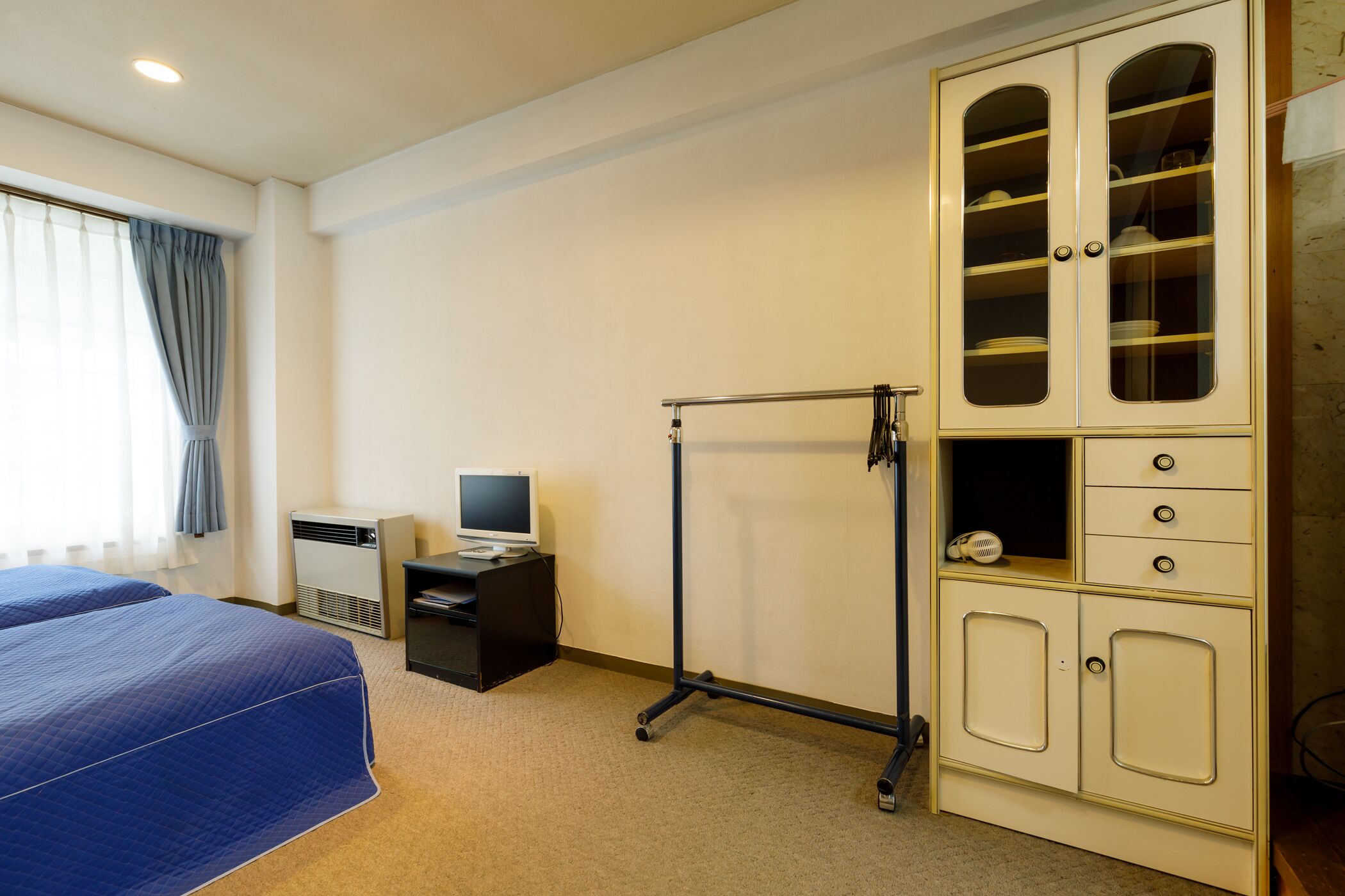 A hotel room with a bed, a desk with a computer, a wardrobe, and a window with curtains.