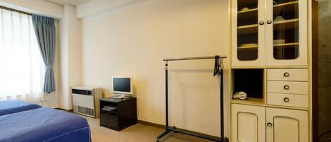 A hotel room with a bed, a desk with a computer, a wardrobe, and a window with curtains.