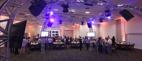 A conference room with a stage, multiple tables, and attendees.