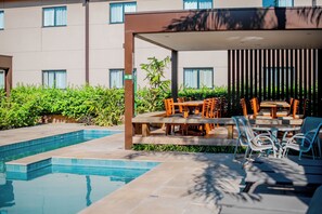 A poolside area with a covered seating area, a swimming pool, and a building in the background. - Fildi Hotel & Eventos (Sumare)