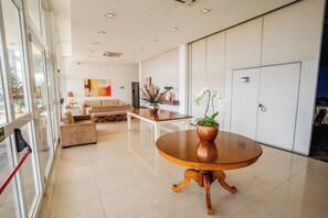 Un hall d’hôtel moderne avec une table ronde en bois, des canapés et une grande fenêtre.