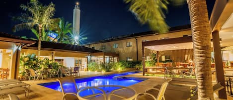 A poolside area with lounge chairs and a swimming pool at night.