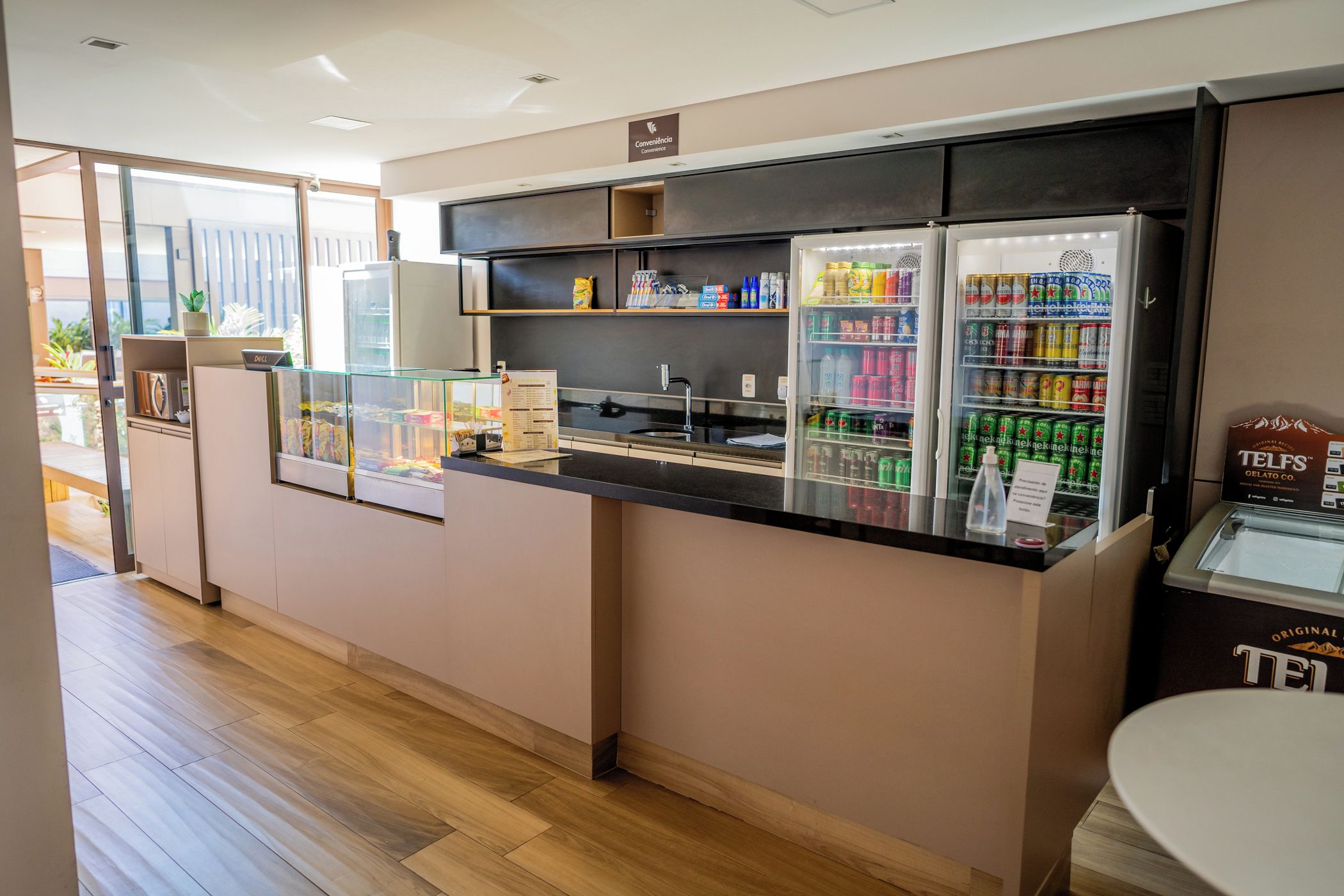 A self-service beverage station with refrigerated drinks and snacks, a Dell computer, and a sign indicating convenience.
