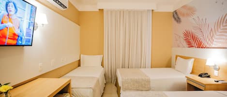 A hotel room with two single beds, a desk with a chair, a television, and a wall-mounted air conditioner.