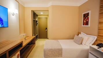 Quarto de hotel com cama, mesa de cabeceira, televisão e escrivaninha com cadeira.