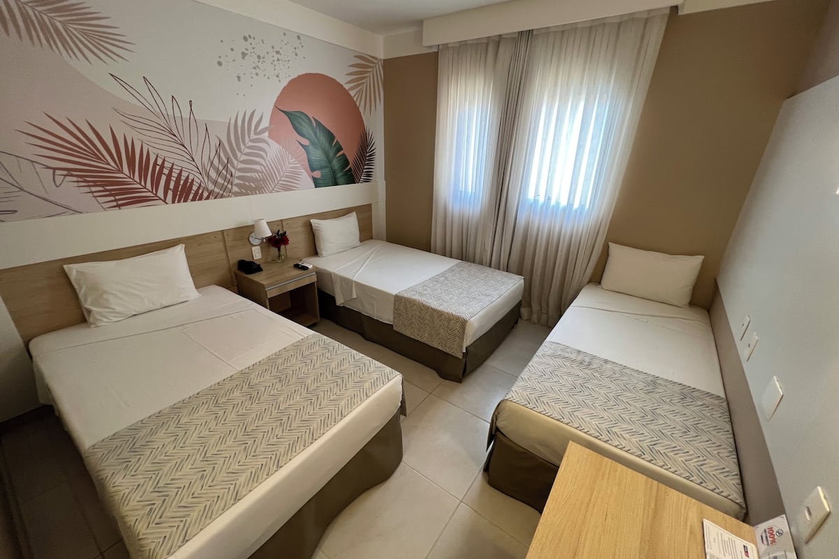 A hotel room with three beds, a wooden nightstand, a small table, and a wall mural.
