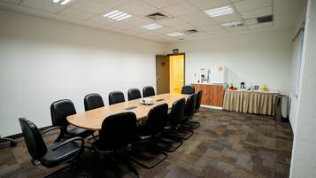 A conference room with a long table, chairs, a projector, and a kitchenette area.