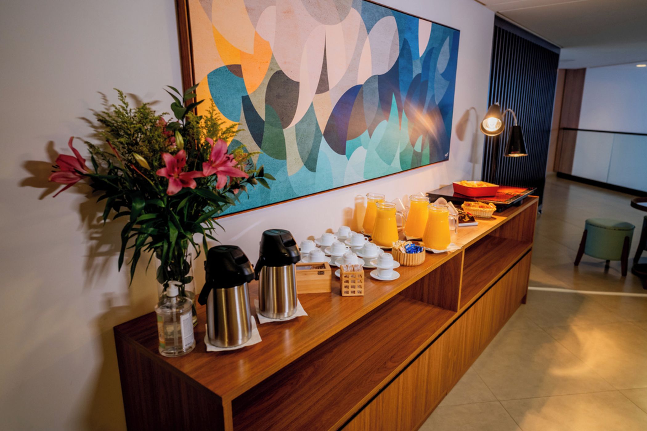 A hotel reception area with a coffee station, a fruit display, and a large abstract painting on the wall.