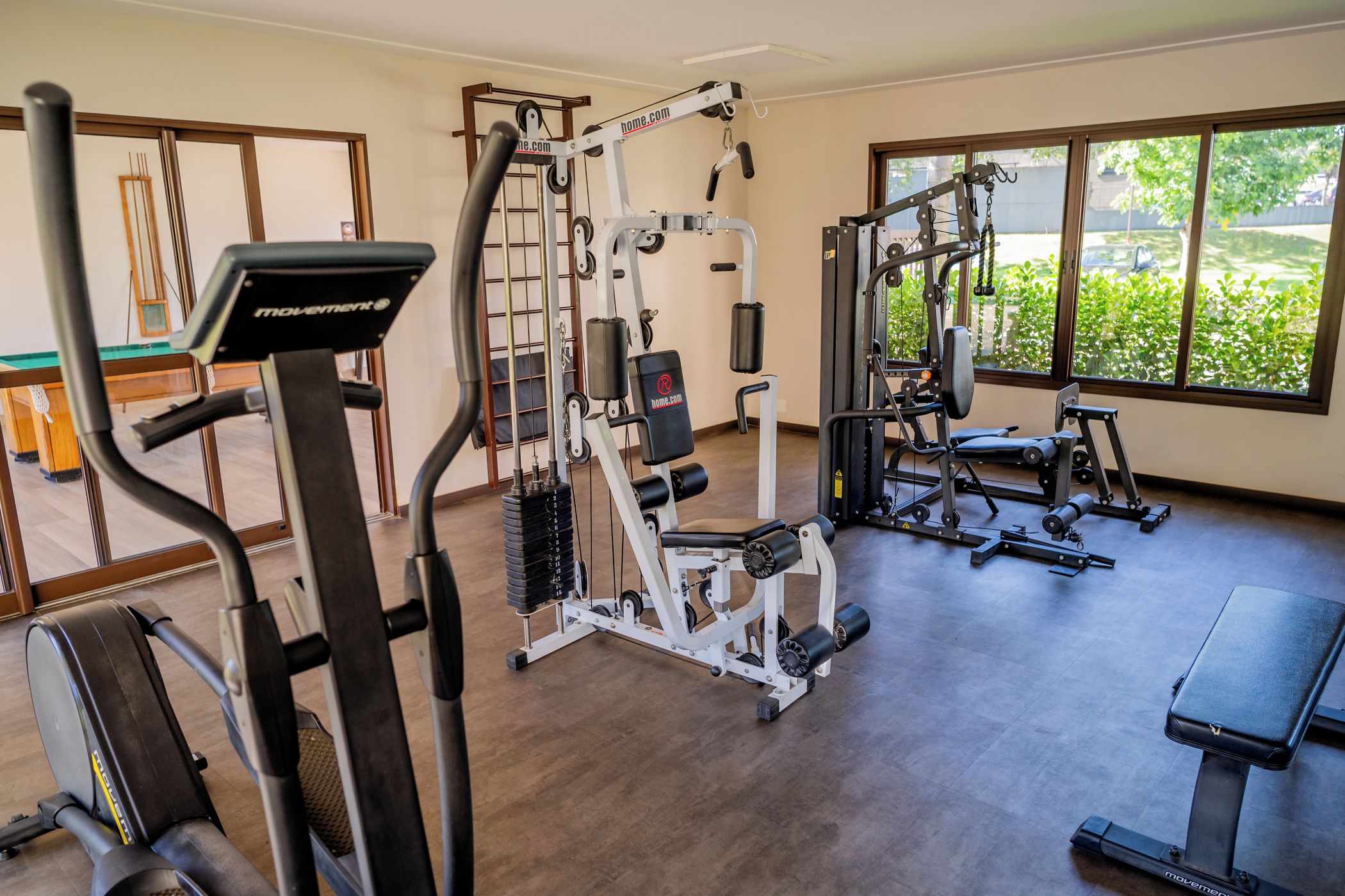 Academia com diversos equipamentos de exercício, incluindo esteira, máquinas de peso e um banco.