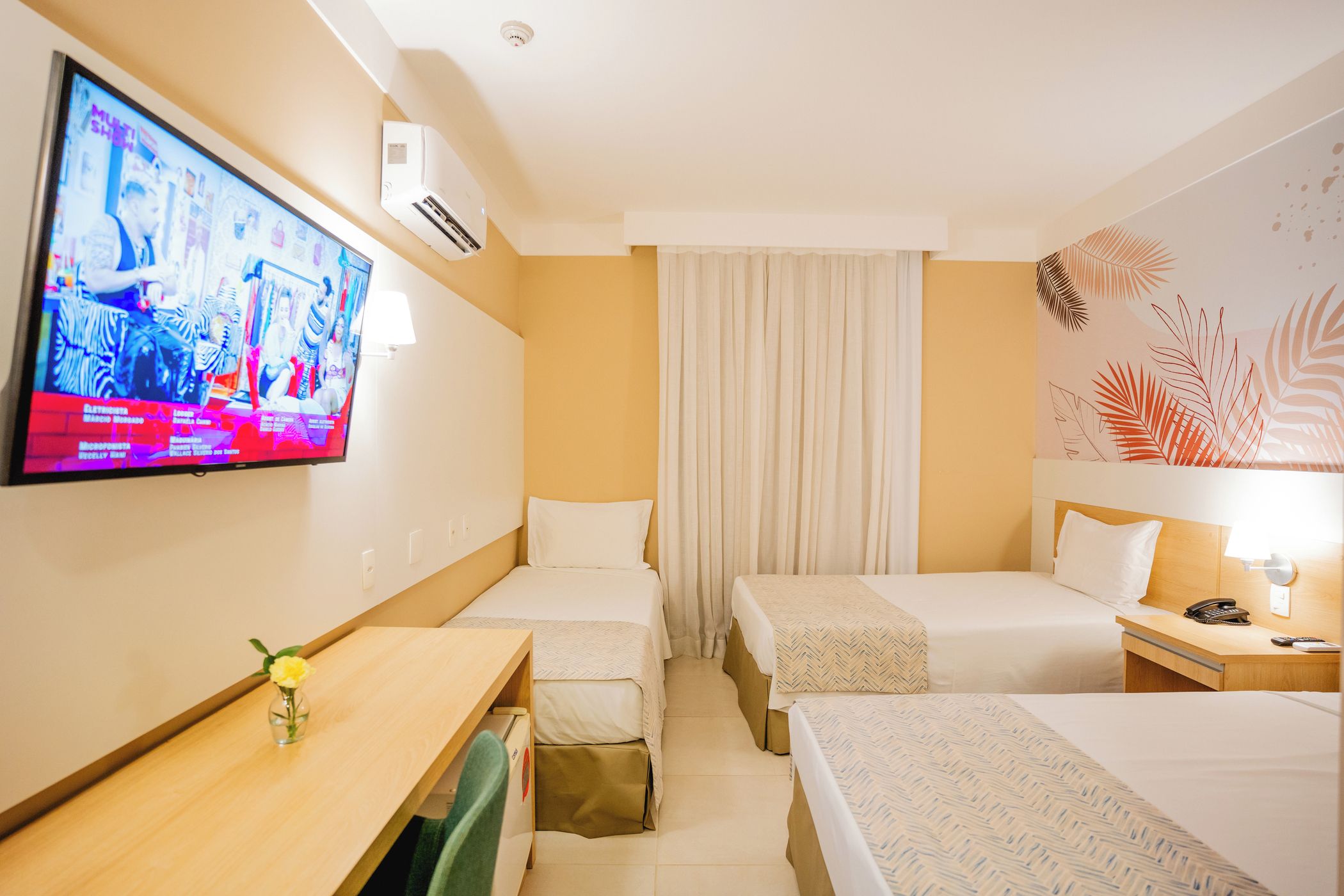 Habitación de hotel con dos camas, un escritorio, un televisor y aire acondicionado instalado en la pared.