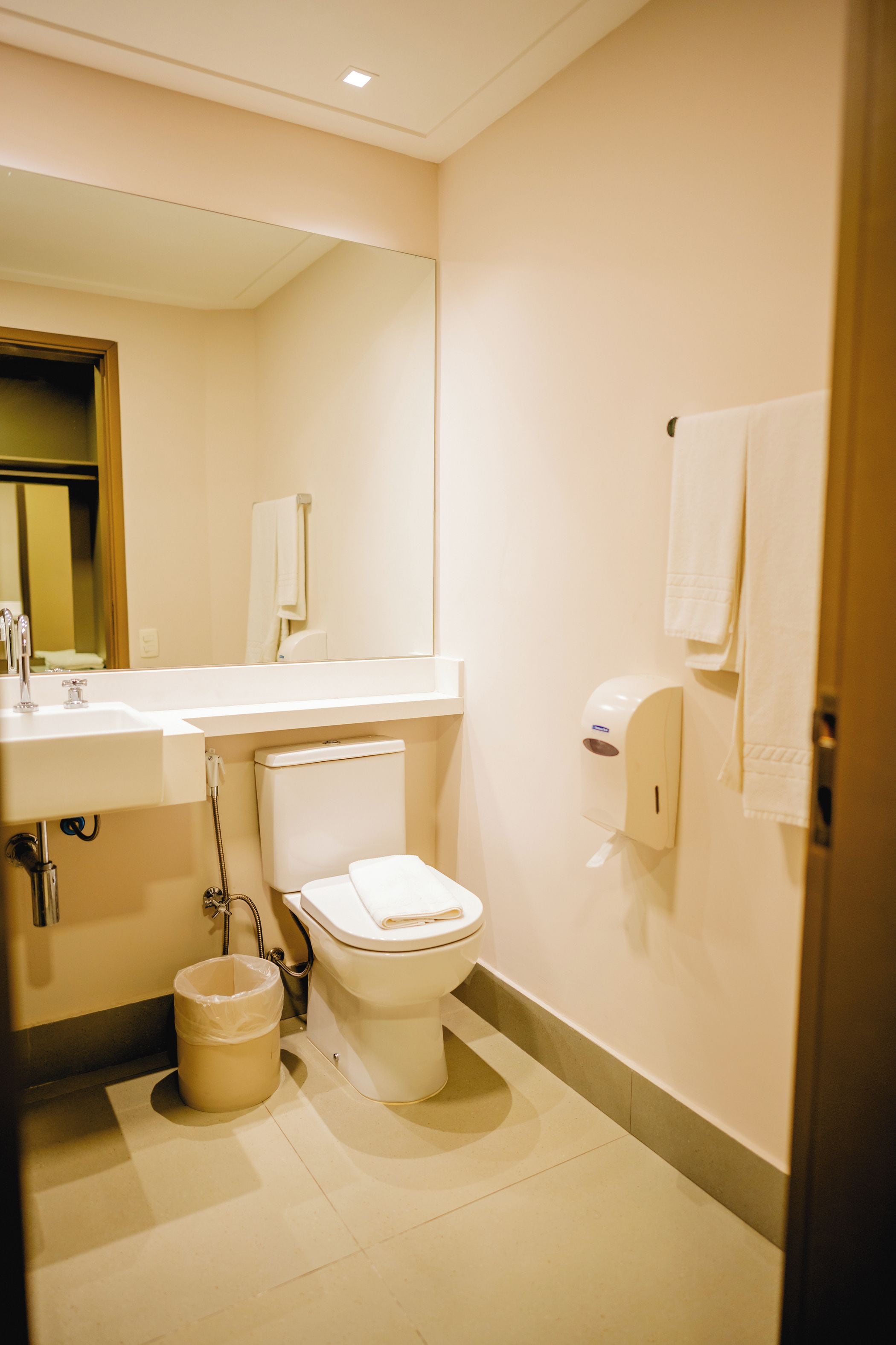 Un baño con inodoro, lavamanos, espejo y dispensador de toallas.