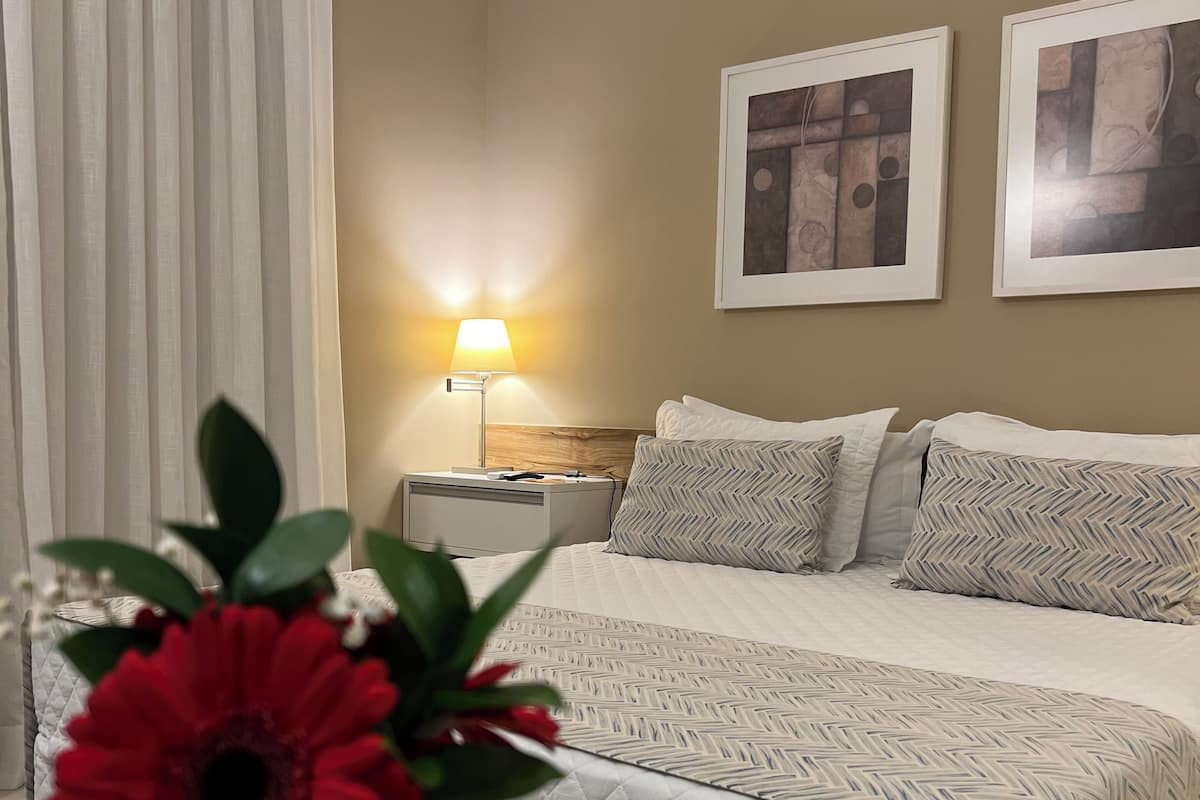 A hotel room with a bed, a nightstand, a lamp, and two framed pictures on the wall.
