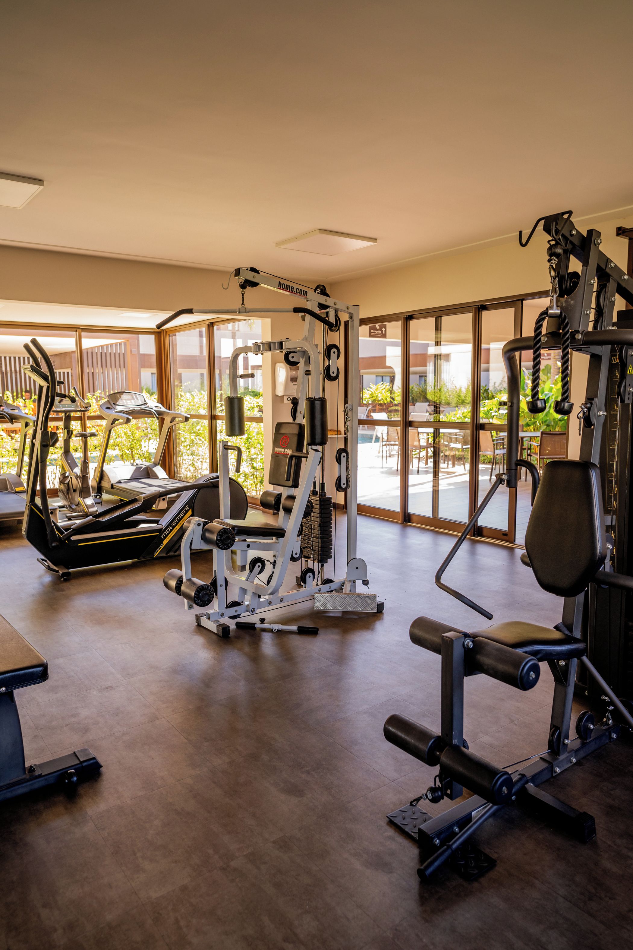 A gym with cardio machines, weightlifting equipment, and a view of a pool and outdoor seating area.