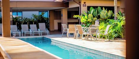 Una piscina con sillones de descanso y un patio cubierto.