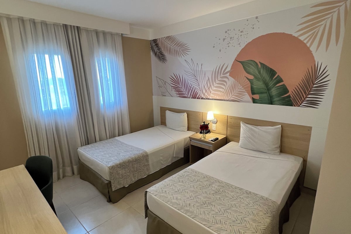 A hotel room with two single beds, a desk, and a nightstand with a lamp.