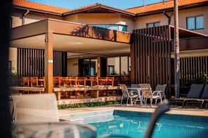 Un espace aménagé au bord de la piscine, comprenant des chaises longues, une piscine et un coin salon couvert avec des tables et des chaises.