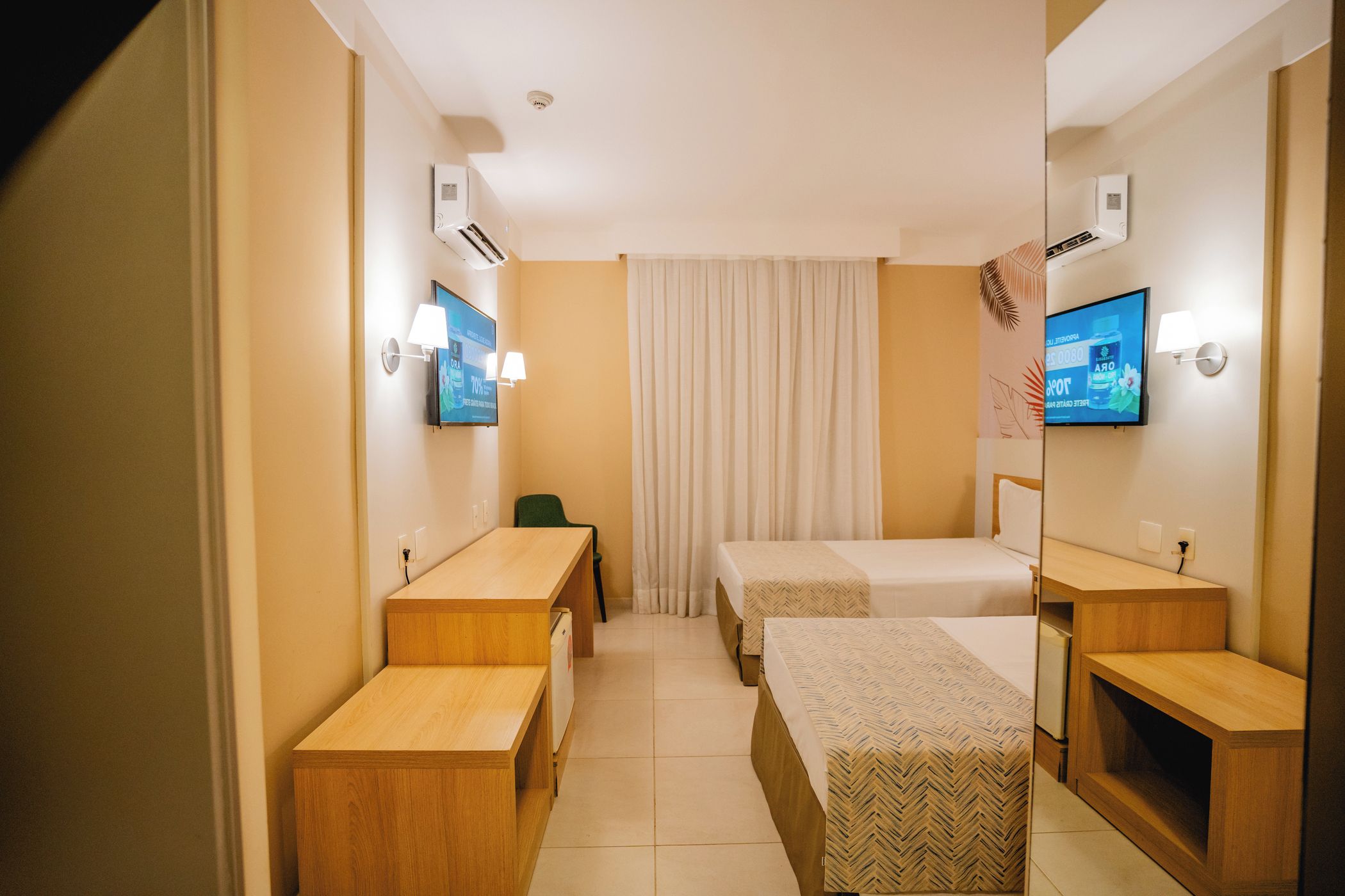 A hotel room with two beds, a desk, a chair, and a television.