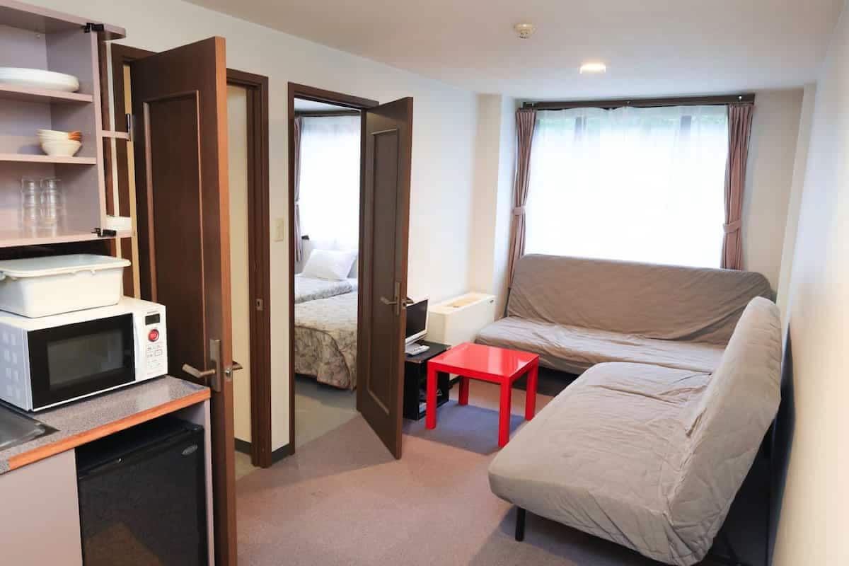 Ein kompaktes Hotelzimmer mit Küchenzeile, einem Bett, einer Schlafcouch und einem kleinen Tisch.