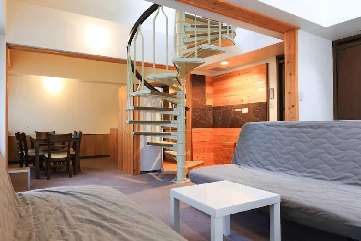 Ein modernes Wohnzimmer mit einer Wendeltreppe, einem Sofa, einem Esstisch und einem kleinen weißen Tisch.