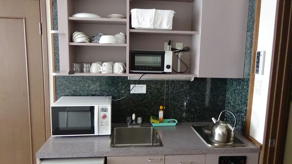 Una cocina compacta con microondas, hervidor y pileta.