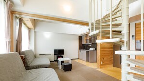 A modern living room with a sofa, a small table, a TV, and a kitchen area with a wooden cabinet and a countertop. - Condominium Hakuba Goryu (Hakuba)