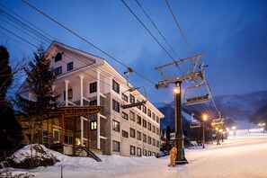 Un hotel moderno con un telesilla, paisajes nevados y montañas al fondo.