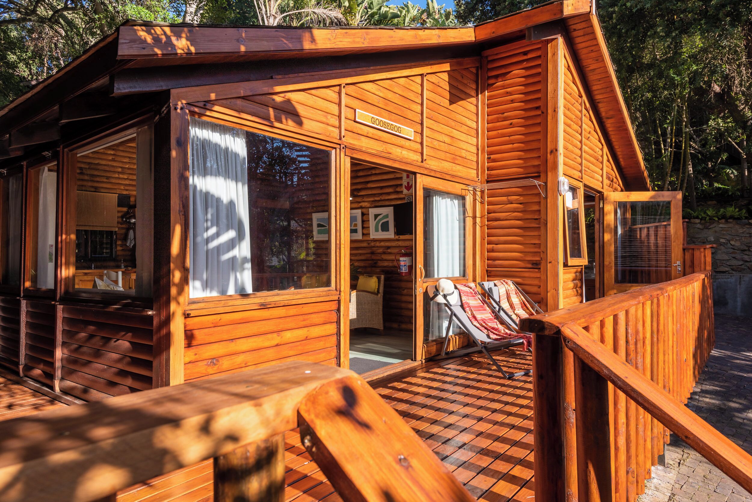 A wooden cabin with a porch, a dining area, and a lounge chair.