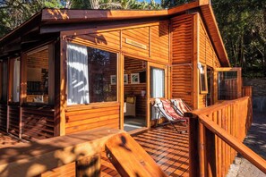 A wooden cabin with a porch, a dining area, and a lounge chair. - Under Milkwood Resort (Knysna)