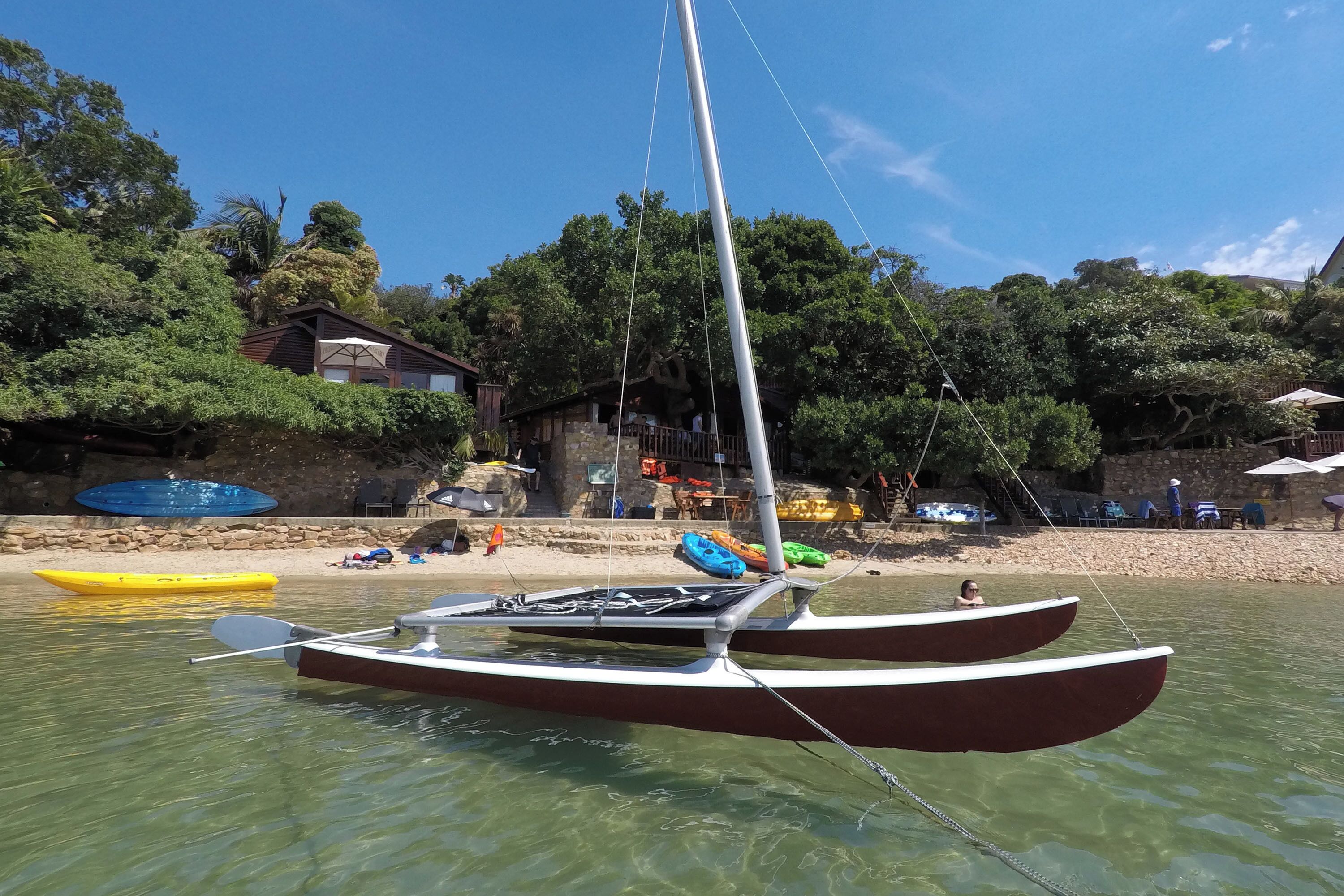 A sailboat docked near a beach with a building in the background.