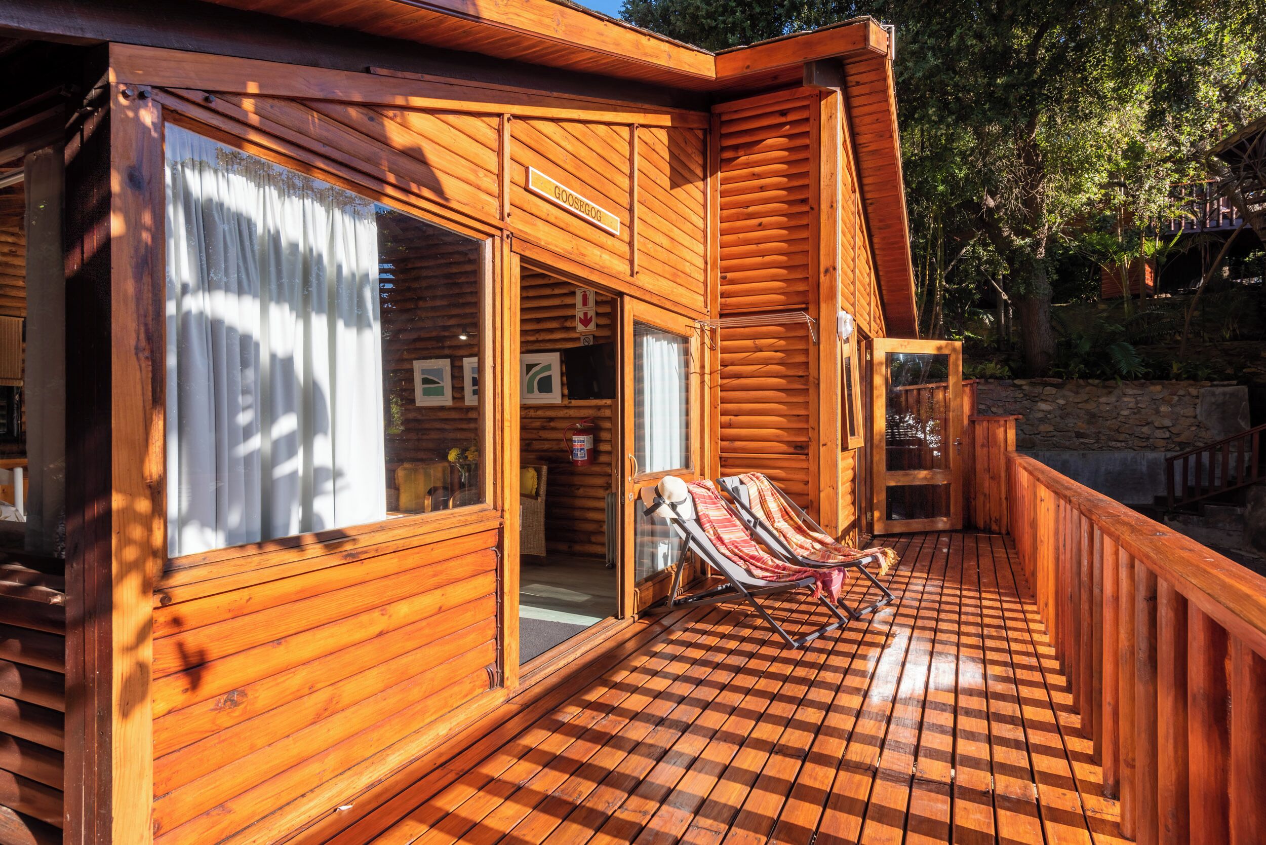 Eine Holzhütte mit Schachbrettfußboden, einer überdachten Terrasse und einem Liegestuhl.