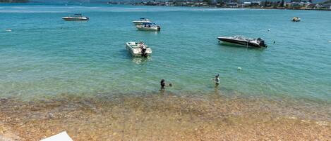 A clear lake with boats, a pebbly shore, and distant hills.