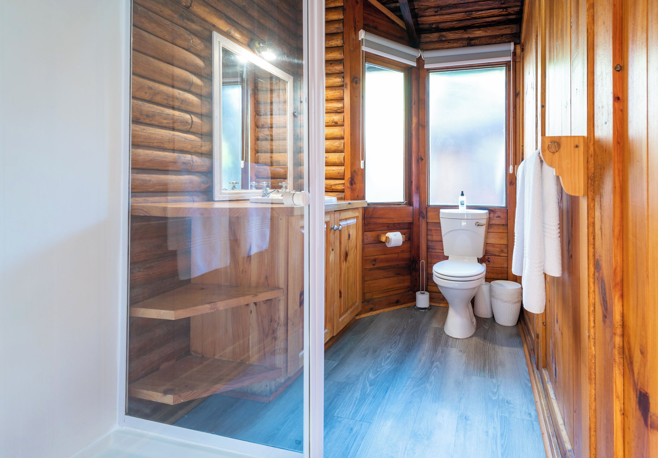 A wooden cabin bathroom with a toilet, sink, and a shower area.
