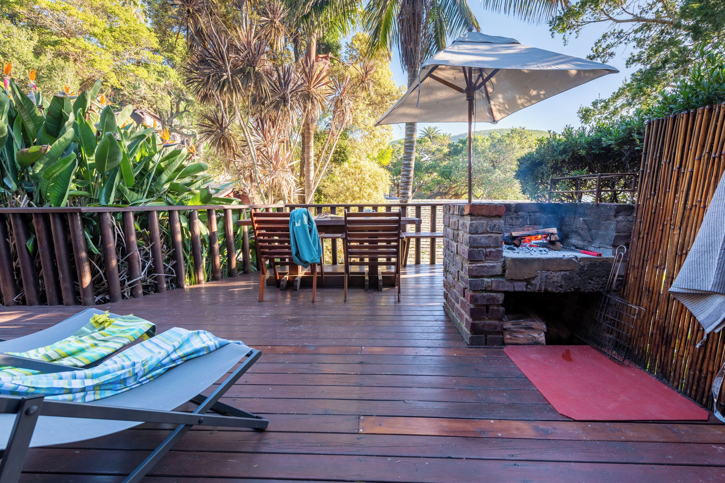 A wooden deck with a barbecue area, a table with chairs, and a lounge chair with a blanket.
