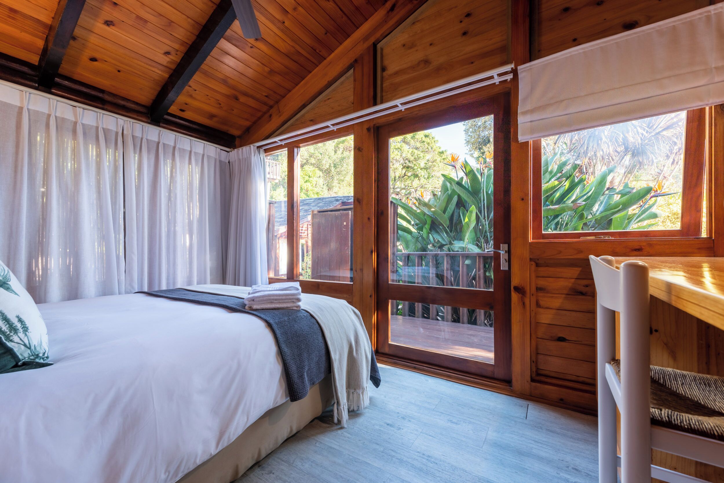A bedroom with a bed, a window with a view of greenery, and a wooden ceiling.
