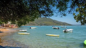 A beach with clear water, boats, and a hilly landscape in the background. - Under Milkwood Resort (Knysna)