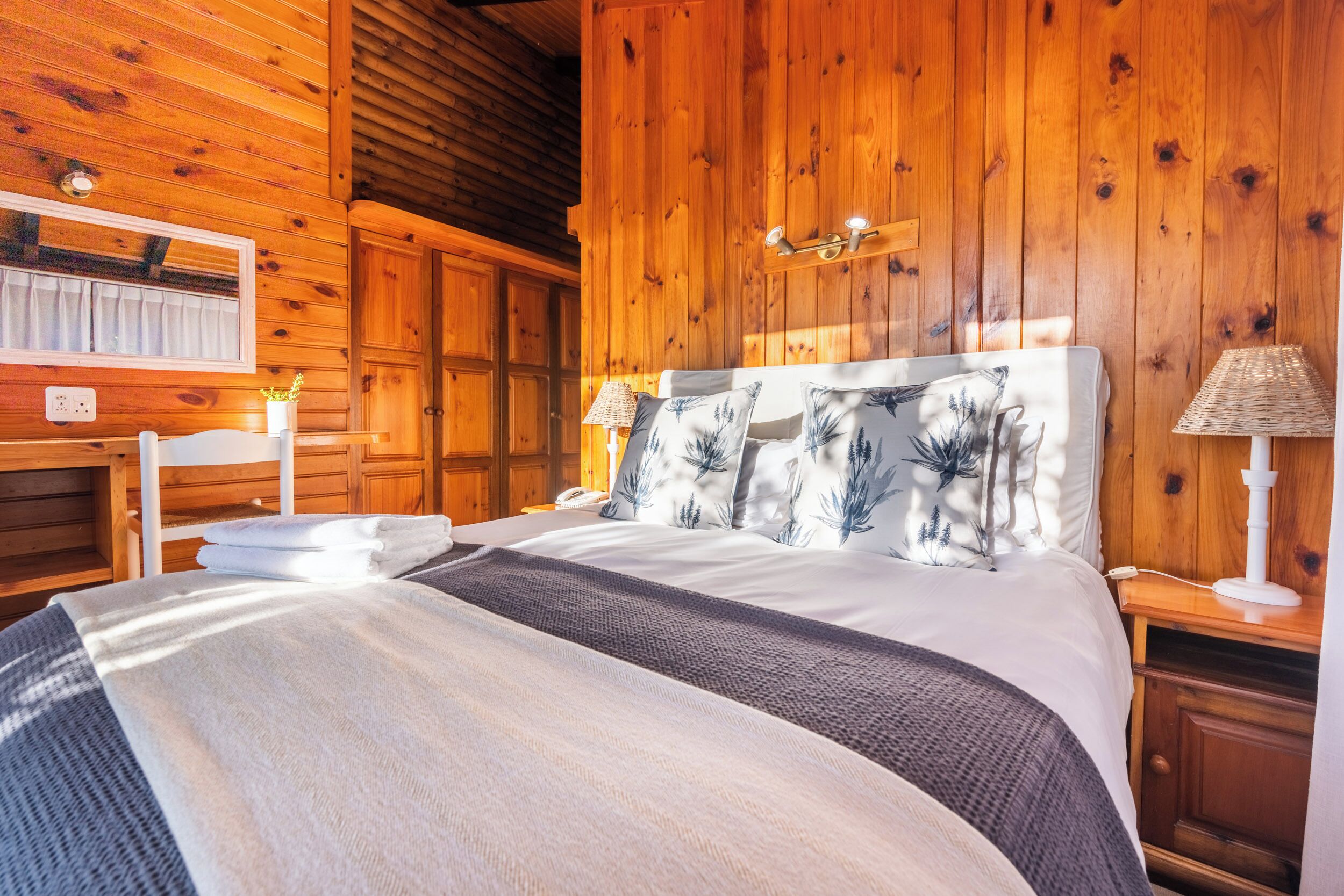 A wooden cabin-style bedroom with a large bed, two bedside tables, a mirror, and a wooden ceiling.