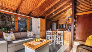 A cozy cabin interior with a wooden ceiling, a dining area, a sofa, and a kitchen. - Under Milkwood Resort (Knysna)